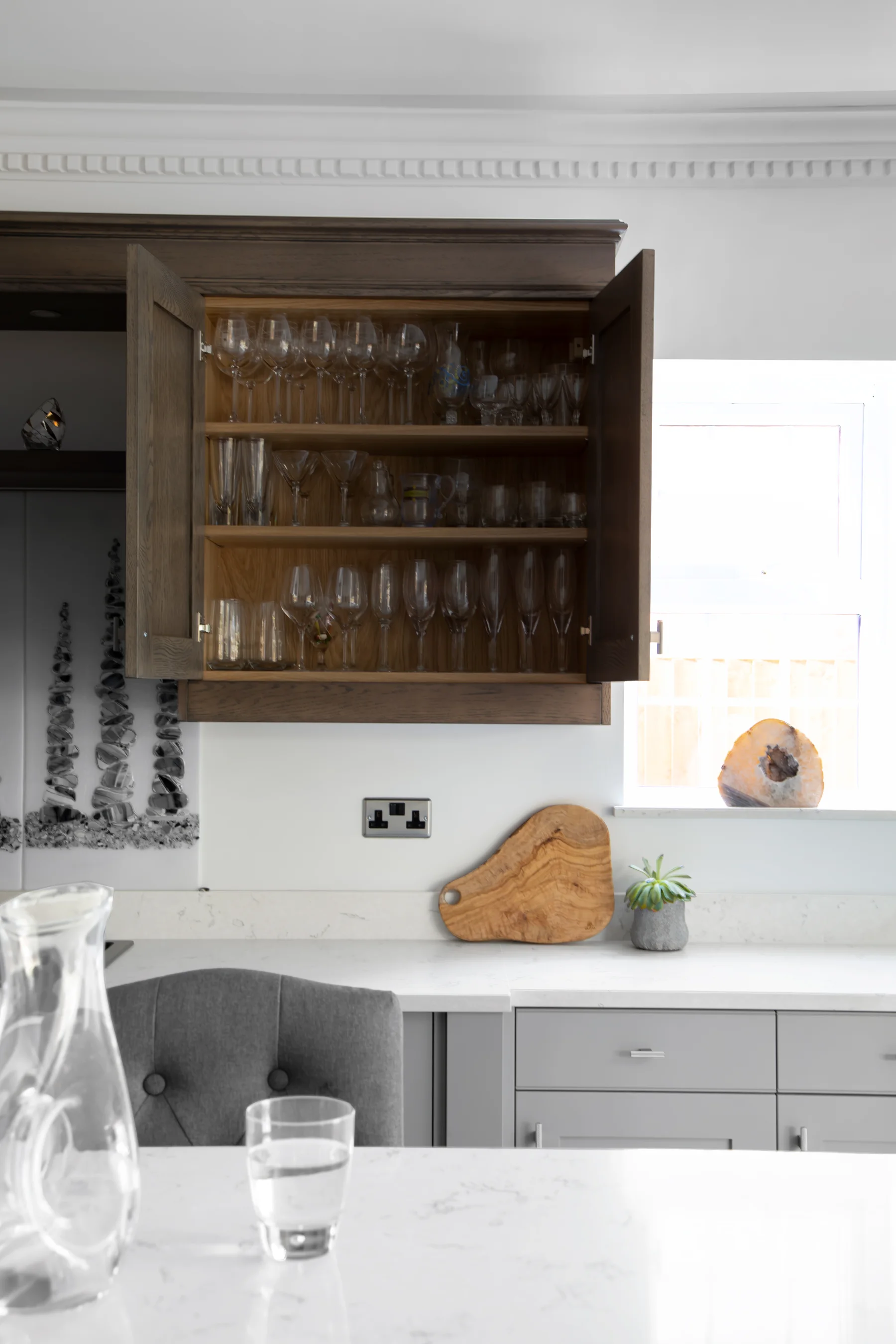 An open dark oak wall cabinet fitted around glassware above a pale work surface