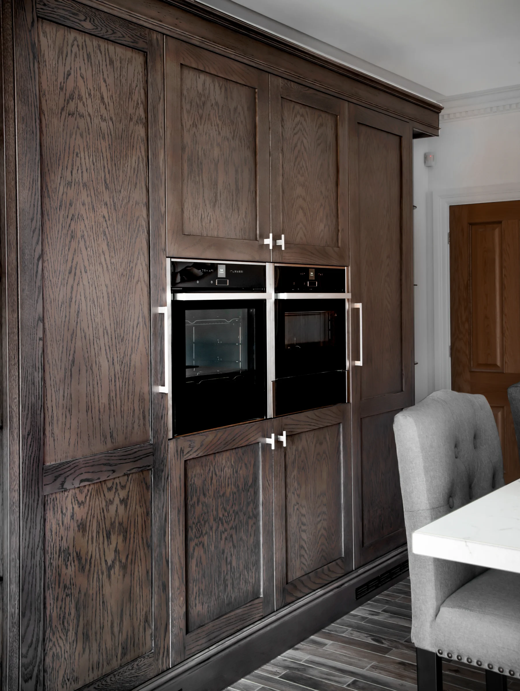 Full-height dark oak kitchen cabinetry with integrated ovens and storage