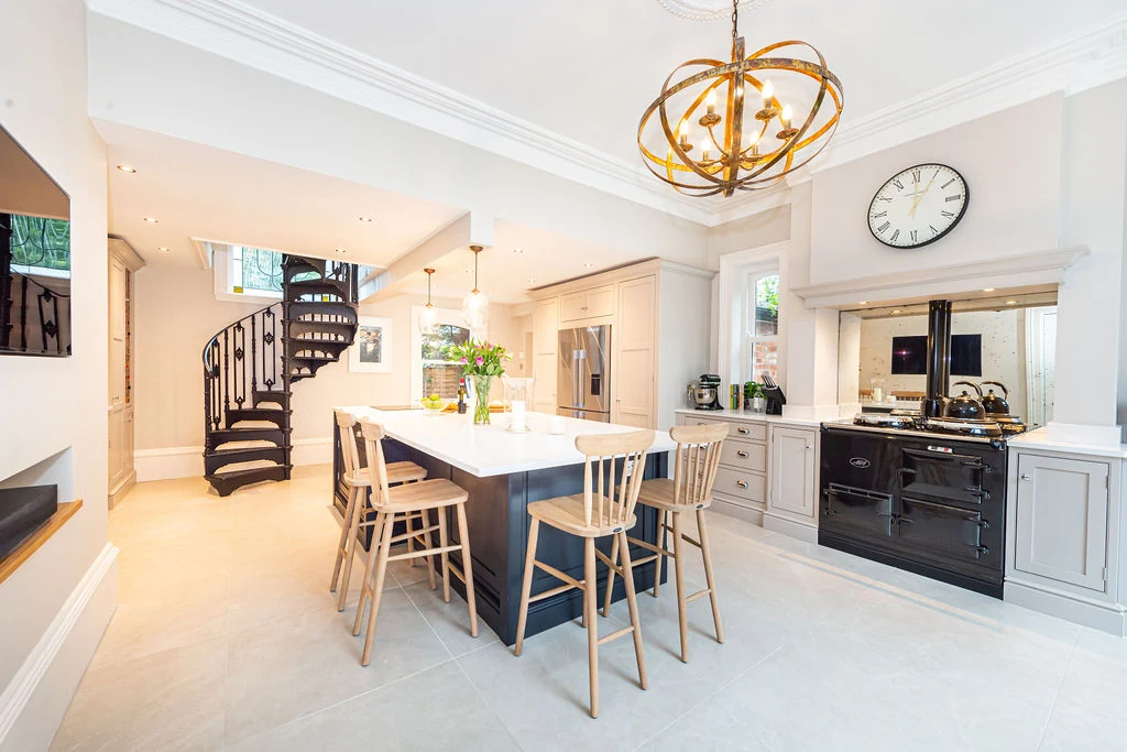 A complete pale painted kitchen arranged around a dark island and range